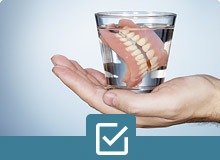 hand holding a glass of dentures